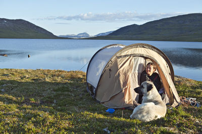 Tourist with dog in tent on lakeshore