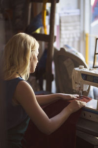 Side view of female fashion designer sewing in studio