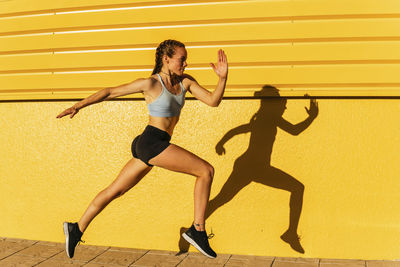 Full length of young woman running against yellow wall