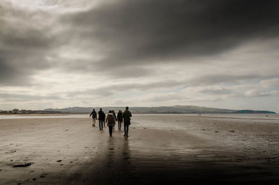 Rear view of people walking at beach against sky