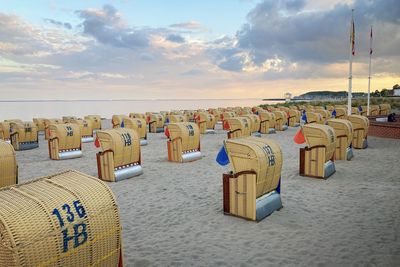 Hooded chairs on beach against sky during sunset