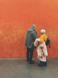 Rear view of people standing against orange wall