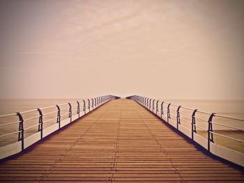 Wooden footbridge over sea against clear sky