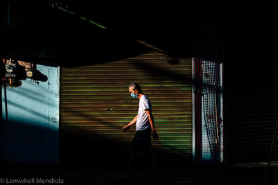 Side view of young man standing against building