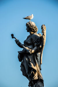 Bird perching on statue against clear blue sky