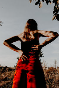 Rear view of woman with hands on hip standing on field against clear sky