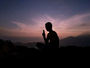 Silhouette man sitting on mountain against sky during sunset