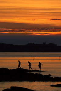 Silhouette people on beach against orange sky