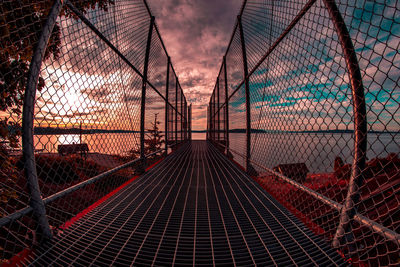 Footbridge over chainlink fence against sky during sunset