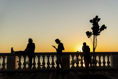 Silhouette people standing by railing against sky during sunset