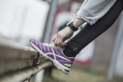 Low section of woman tying lace of sports shoe on railing