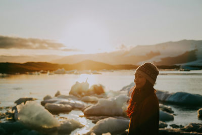 Side view of woman looking at beach against sky during sunset
