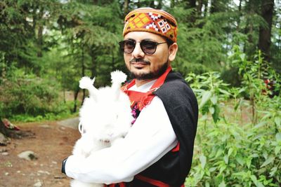 Portrait of young man wearing traditional clothes while holding rabbit outdoors