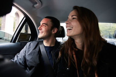 Smiling male and female friends looking through window while riding in car