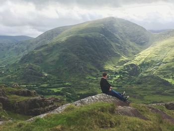 Woman sitting on mountain against sky