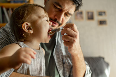 Father feeding porridge with spoon to son at home