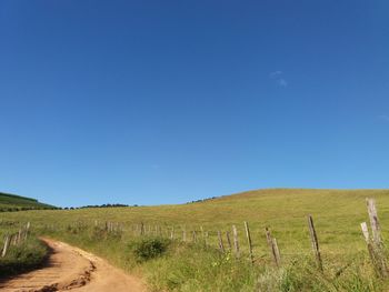 Dirt road amidst field against blue sky