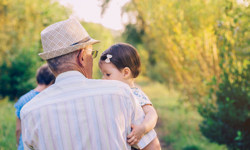 Rear view of grandfather carrying granddaughter while standing at park