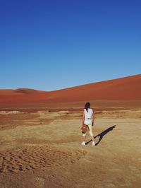 Full length of woman walking at desert against clear blue sky