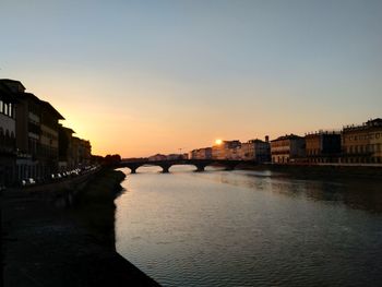 Bridge over river by buildings against sky during sunset