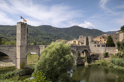 Arch bridge over river by buildings against sky