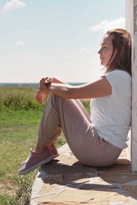 Young beautiful woman sitting next to a wall and enjoying sea scape. summer holiday, relaxation. 