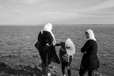 Rear view of women on sea shore against sky