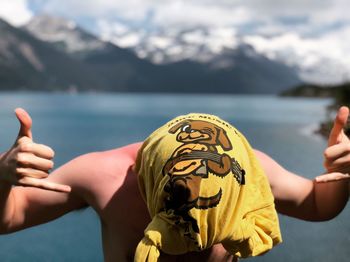 Man head wrapped in towel while gesturing horn sign against lake