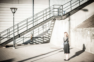 Full length of woman standing by steps on sunny day