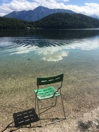 Empty chairs by lake against mountains
