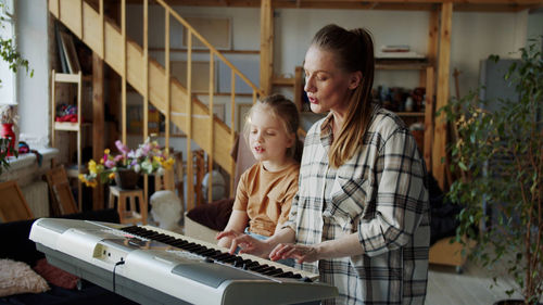 Mother teaching piano to daughter at home