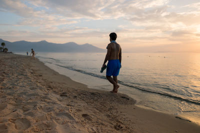 Rear view full length of man walking on shore at beach during sunset