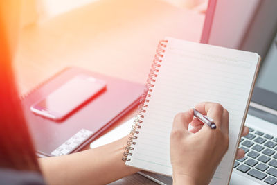 Midsection of businesswoman writing on spiral notebook by laptop in office