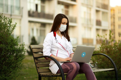 Young woman using phone while sitting on bench at park