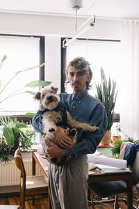 Portrait of male architect carrying dog standing at home office