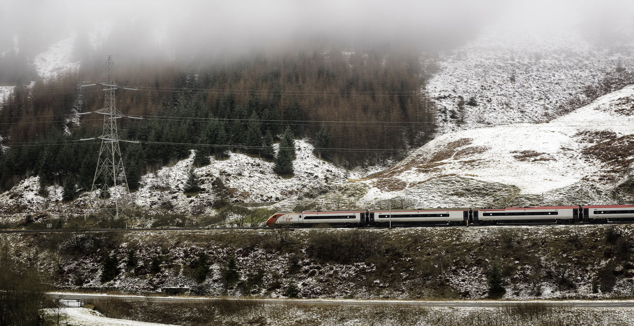 TRAIN ON RAILROAD TRACK BY MOUNTAINS