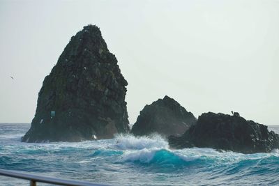 Rock formation in sea against clear sky