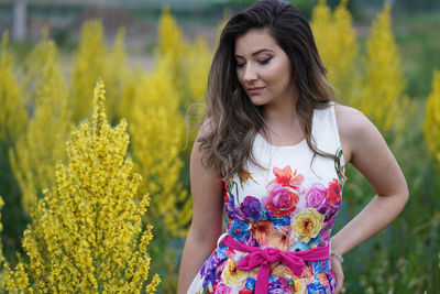 Beautiful young woman standing against yellow flowering plants