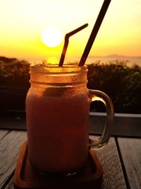 Close-up of drink in glass jar on table against sunset background