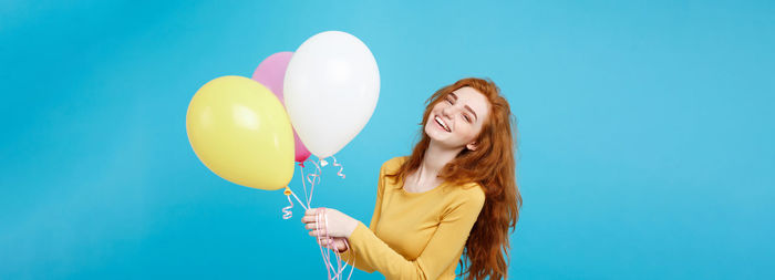 Portrait of young woman holding balloon against blue background