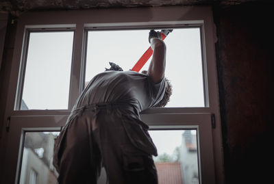 A construction worker is repairing a window frame from the outside. person