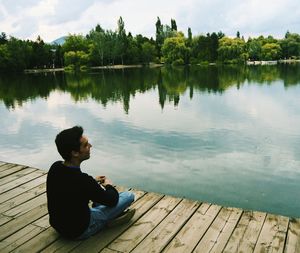 Side view of man sitting on pier over lake