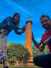 Happy friends smiling while holding umbrella against trees