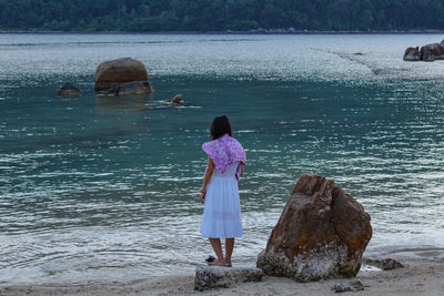 Rear view of woman standing on rock by river