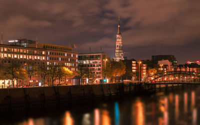 Illuminated city by river against sky at night