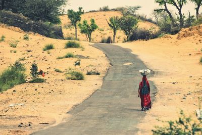 Rear view of woman walking on road at field