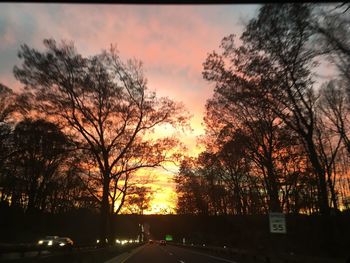 Silhouette trees by road against sky during sunset