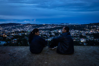 Young couple watching downtown city view with dramatic cloudy sky at evening from mountain top