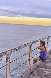 Young woman sitting on pier against sky during sunrise