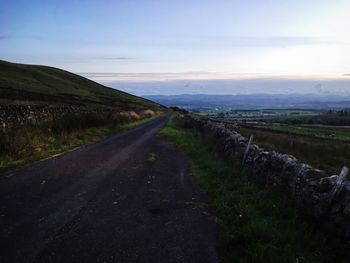 Empty road amidst field against sky